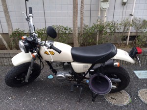 白色のホンダ・エイプ50が屋外に駐車されている。リアには荷物が掛けられており、日常的に使われていたことが感じられる。