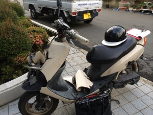 フロント部分が破損し、内部構造が見える状態のJOG、駐車場で撮影