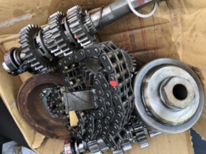 箱の中にまとめられたFLSTC1340のトランスミッション関連部品。ギアやカムチェーン、各種金属パーツが入り乱れた状態で収められている。