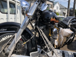 ハーレーFLSTC1340を正面寄りの角度から撮影。車体は分解され、一部パーツが取り外された状態で、運搬用のベルトでしっかり固定されている。