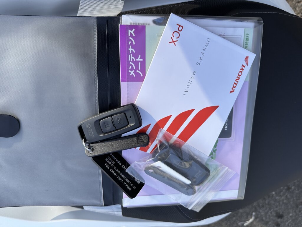 ホンダPCX125の付属品として、取扱説明書、スマートキー、メンテナンスノートなどが一式揃っている写真。
